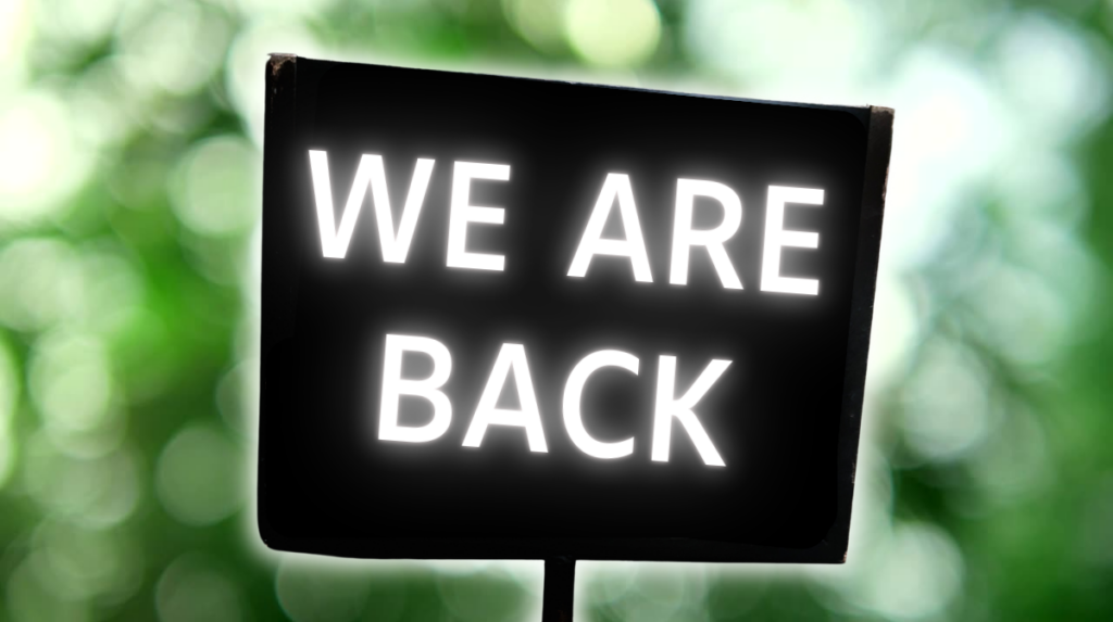 Pancarte noire sur un fond de verdure avec la mention "We are back"